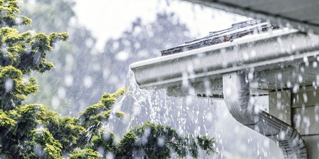 A house with water dripping from its gutter, emphasizing the need for regular gutter cleaning to avoid roof damage.