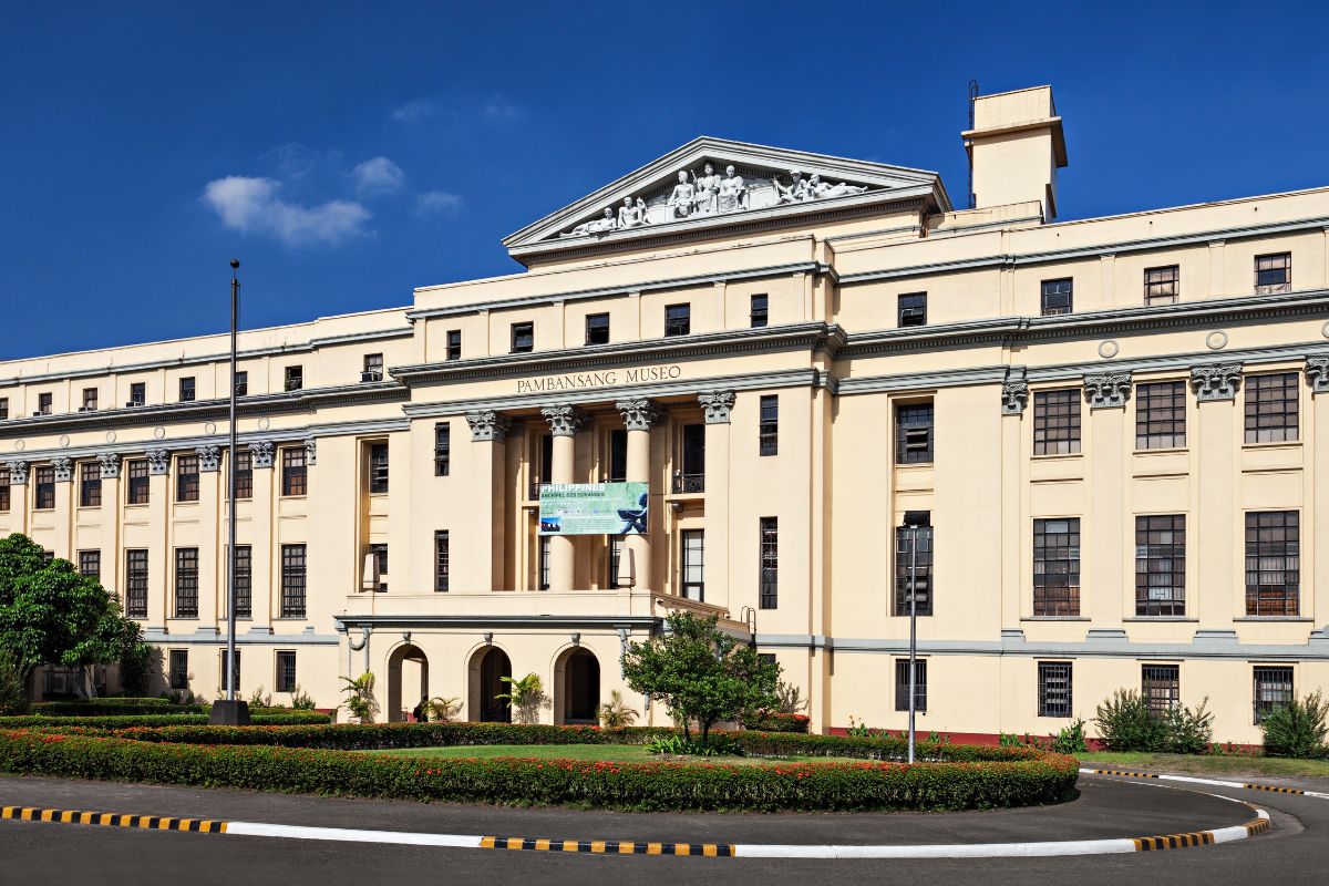 Exterior view of the Pambansang Museo, showcasing its grand architecture against a clear blue sky, surrounded by greenery.
