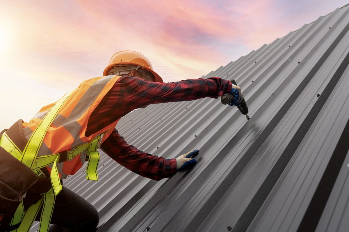 A man in safety gear is installing panels on a metal roof, demonstrating proper safety measures while working at height.