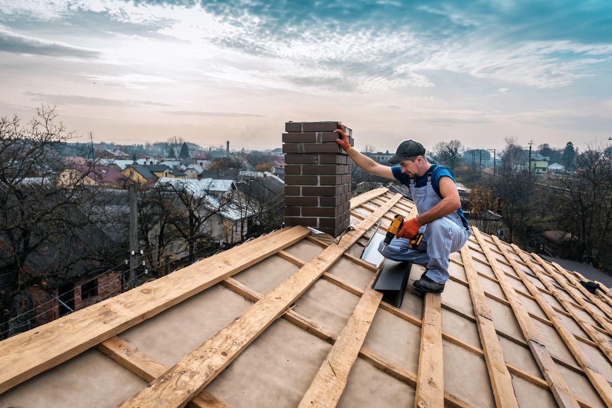A man using a saw to cut materials while working on a roof, wearing safety gear and focused on his task.